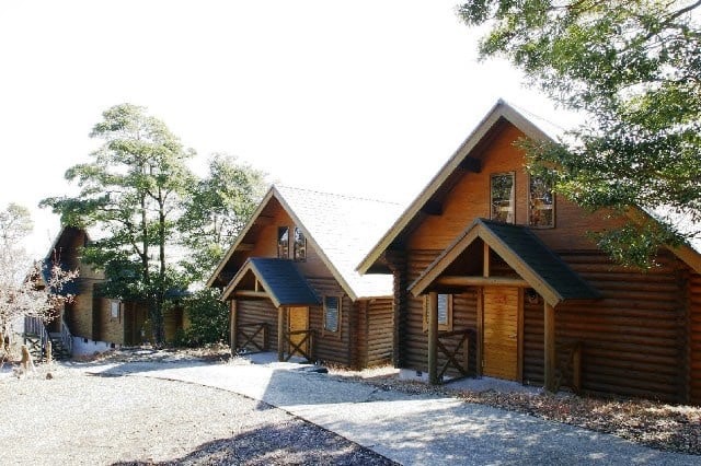 横岳自然公園のキャンプ場に建つ木造のロッジ風コテージ。木々に囲まれた自然豊かな環境で、コテージが並んでいる。